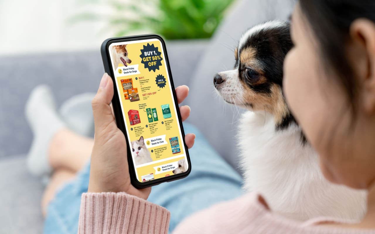 A woman holding a small dog and a phone with the the black friday flyer on the screen