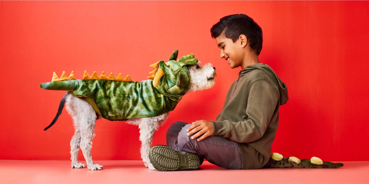 A happy dog wears a matching Dinosaur costume with the child owner